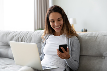 Laechelnde Frau auf Sofa mit Laptop und Handy am onlineshoppen