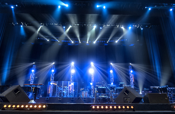 a blue-lit concert stage with trusses, instruments and loudspeakers.